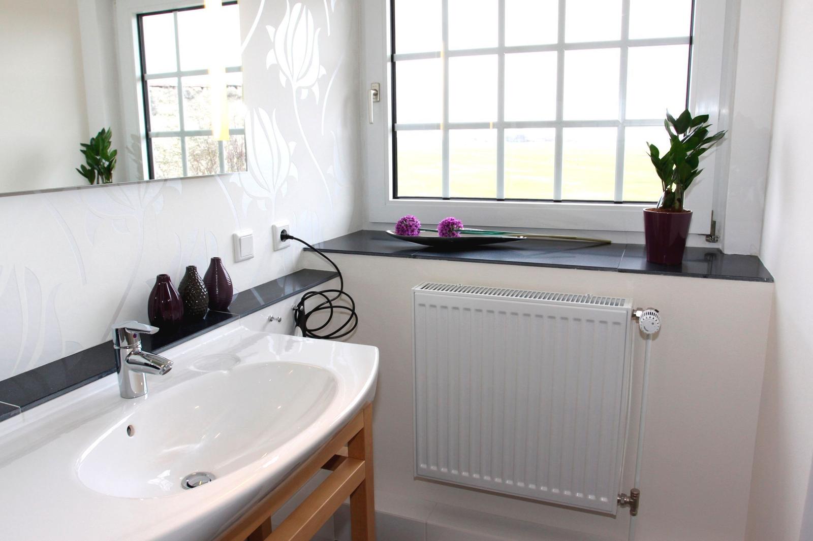 Badezimmer mit Waschbecken, Spiegel und Fenster mit Pflanze.