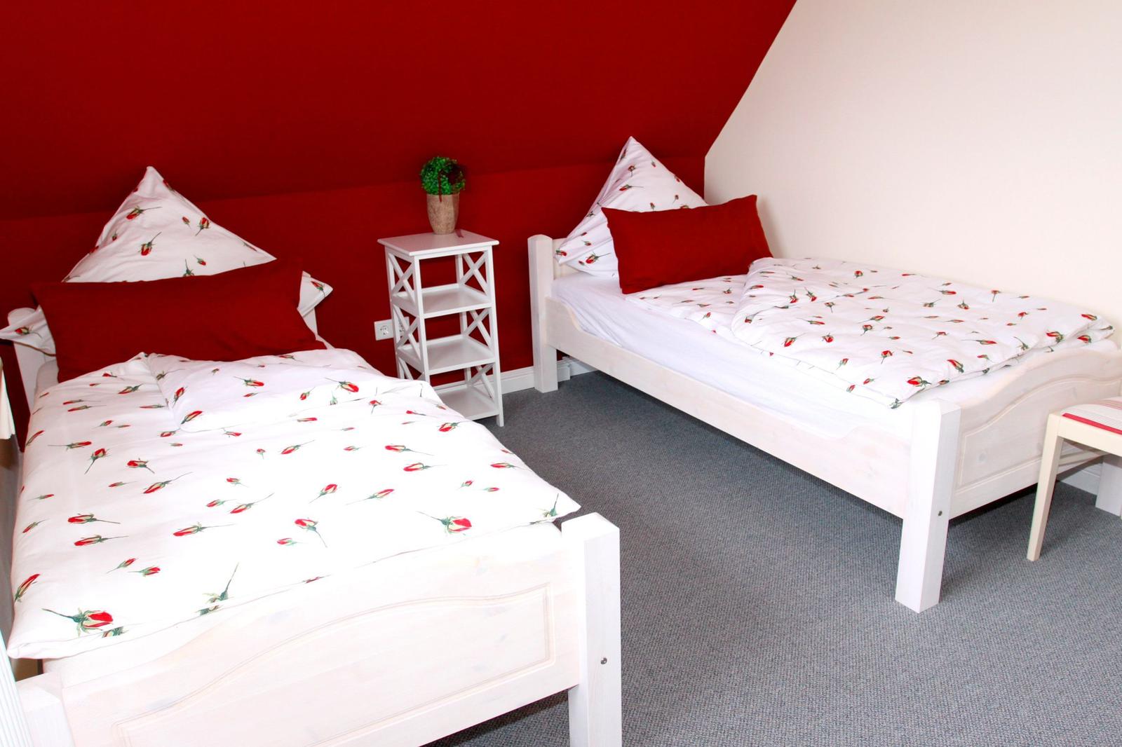 Zwei weiße Einzelbetten mit rosafarbenem Bettzeug und roten Kissen.