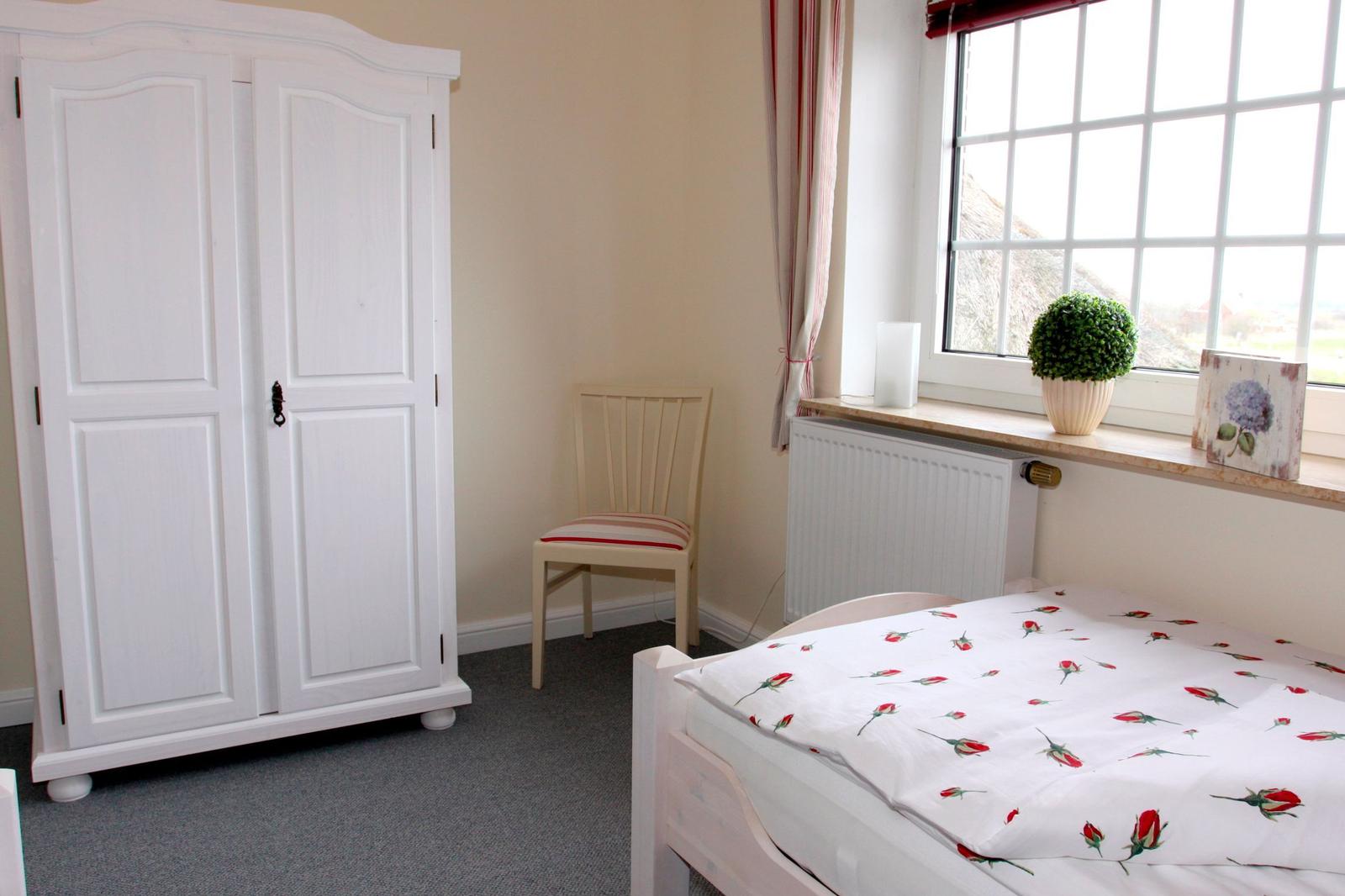 Schlafzimmer mit Bett, Kleiderschrank und Stuhl. Fenster mit Pflanze und Deko.