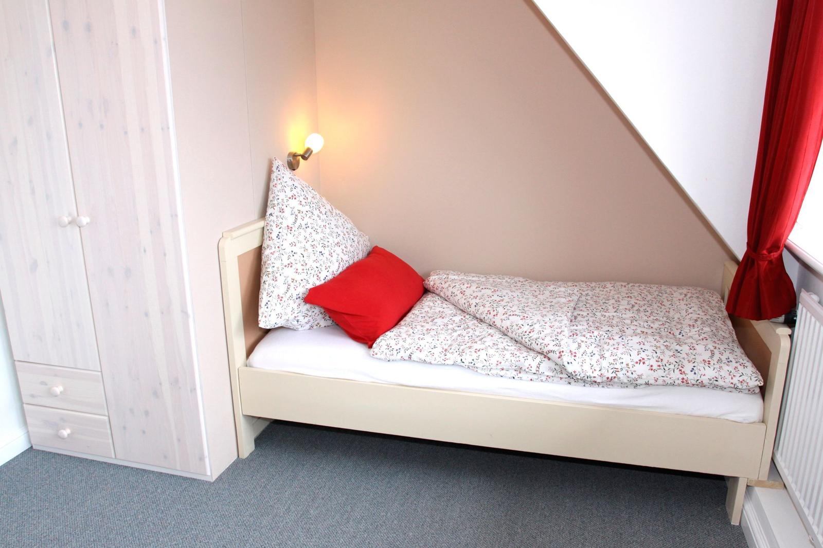 Ein Bett mit Blumenbezug und rotem Kissen unter einem Dachfenster mit rotem Vorhang.