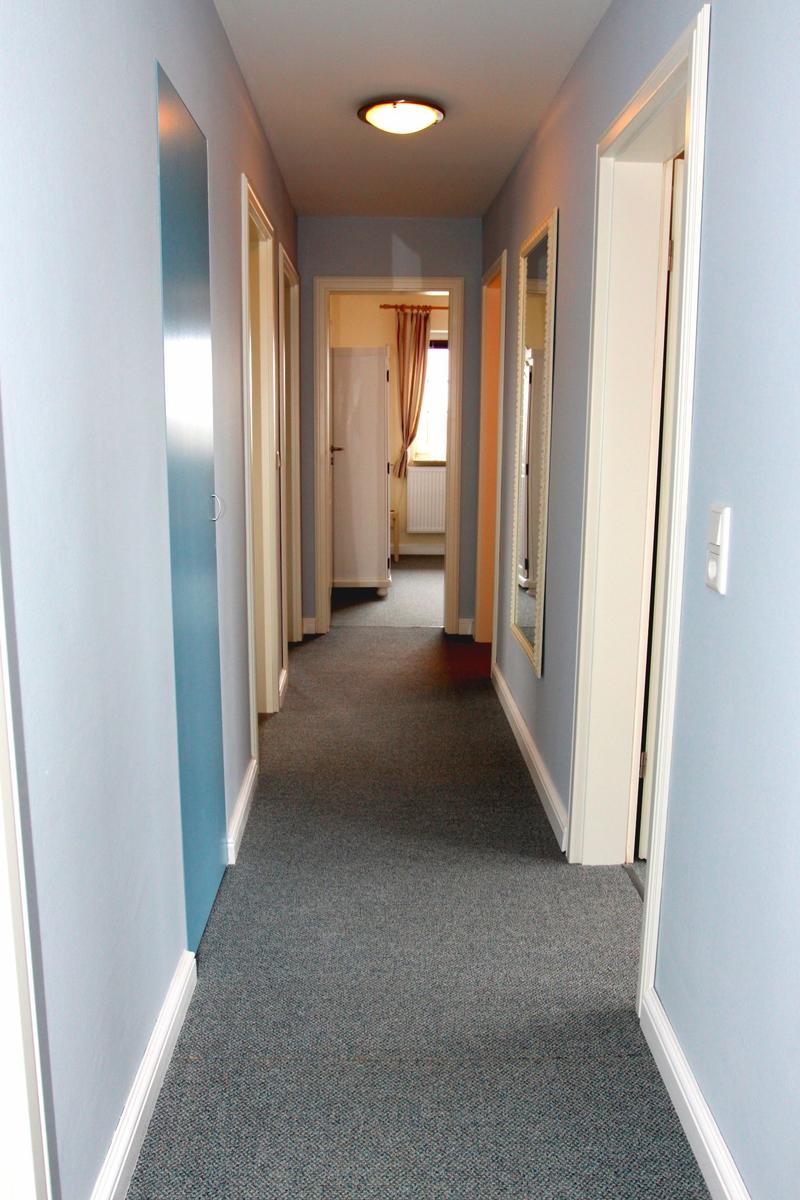 Flur mit blauen Wänden und grauem Teppichboden. Türen und Spiegel sind sichtbar.