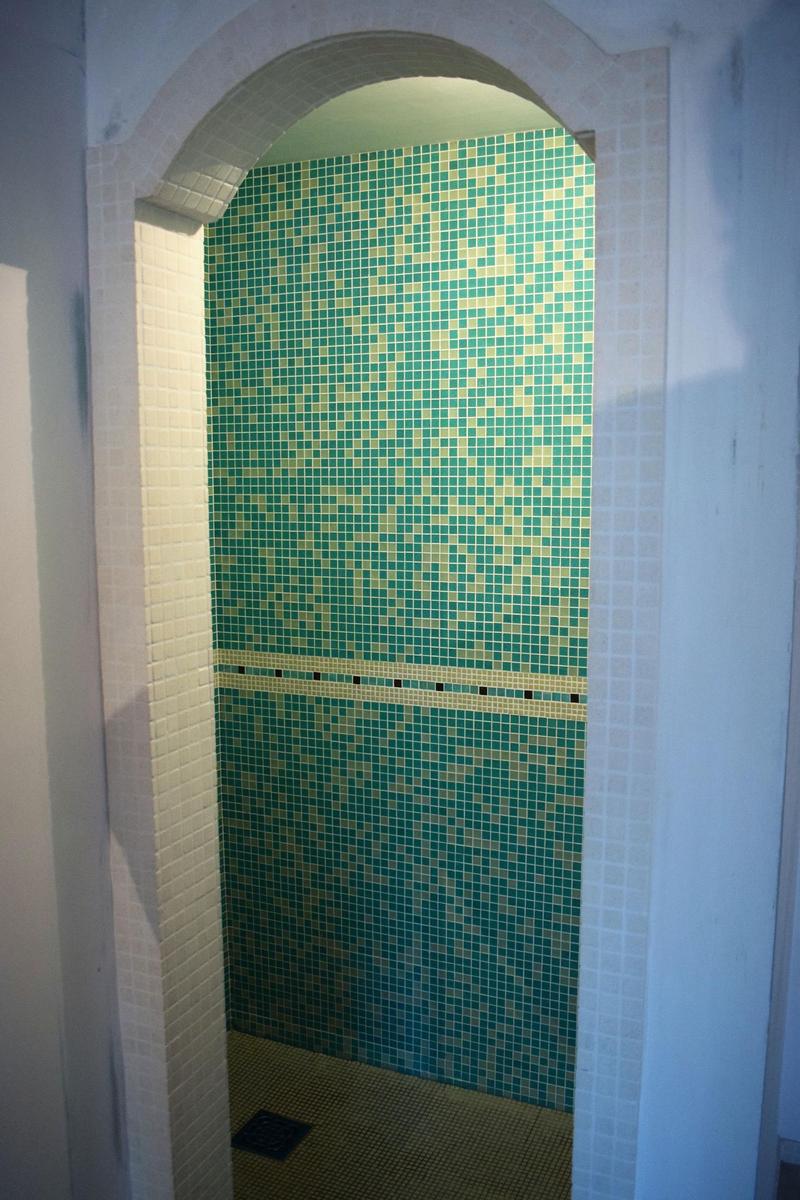 Duschkabine mit grün-gelben Mosaikfliesen und weißem Bogenrahmen.