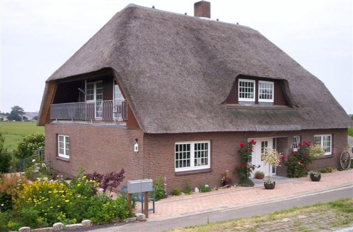 Haus mit Strohdach, Balkon und Blumenbeet vor der Tür