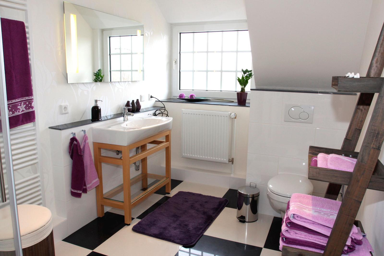 Badezimmer mit Waschbecken, Toilette und Duschbereich. Schwarze und weiße Fliesen.