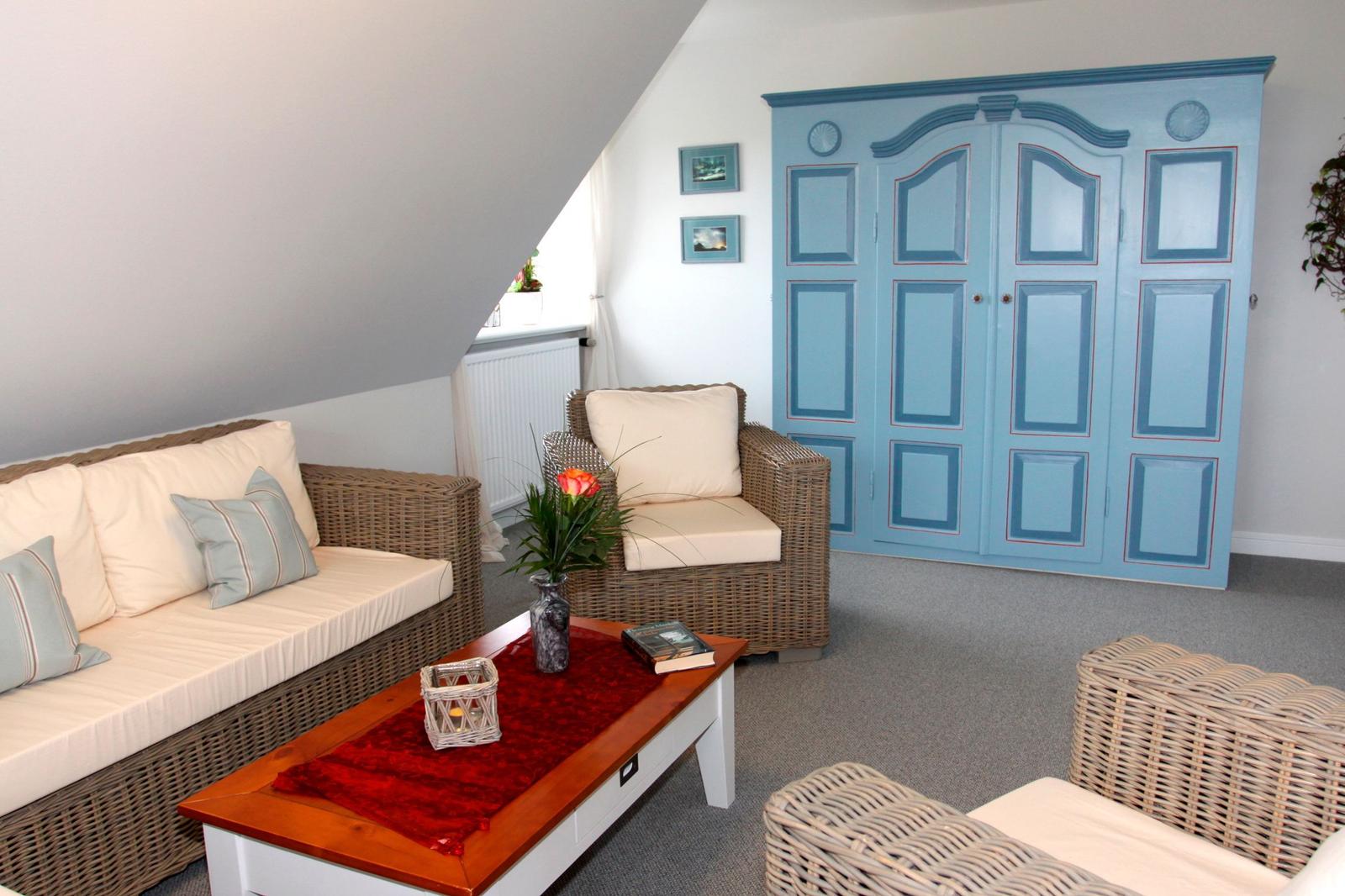 Wohnzimmer mit blauem Schrank, Wickermöbeln und Holztisch.