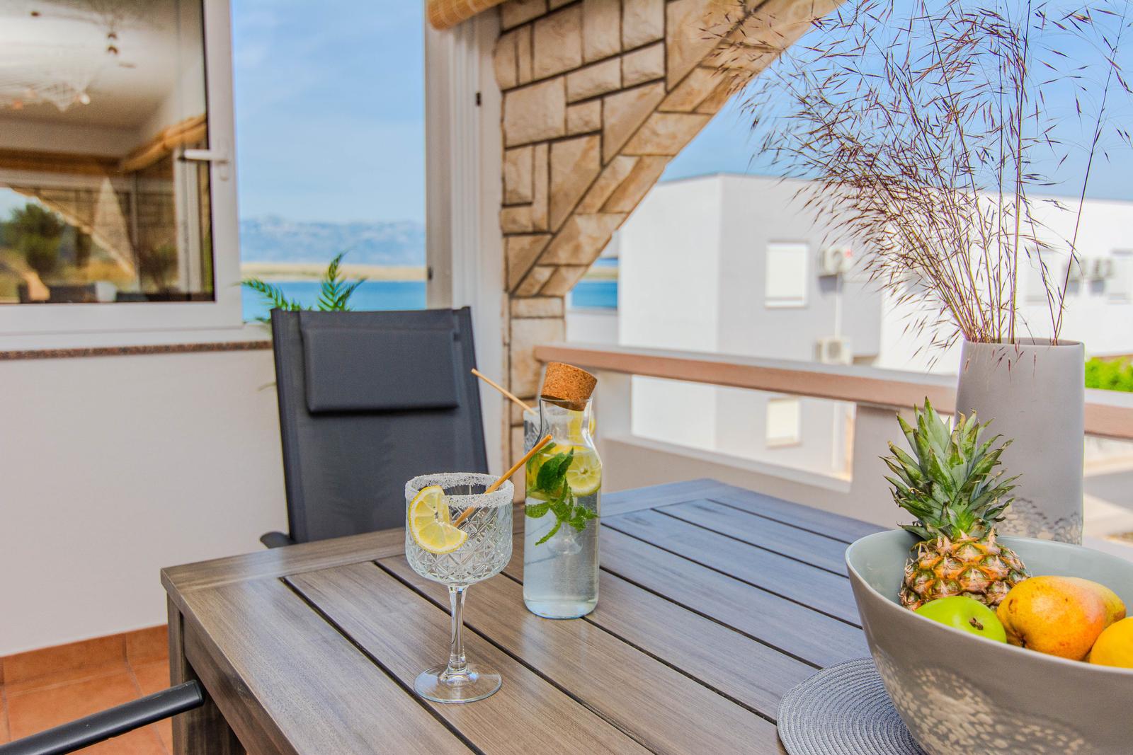 Terrasse mit Tisch, Stuhl und Obst. Blick auf Meer und Himmel.