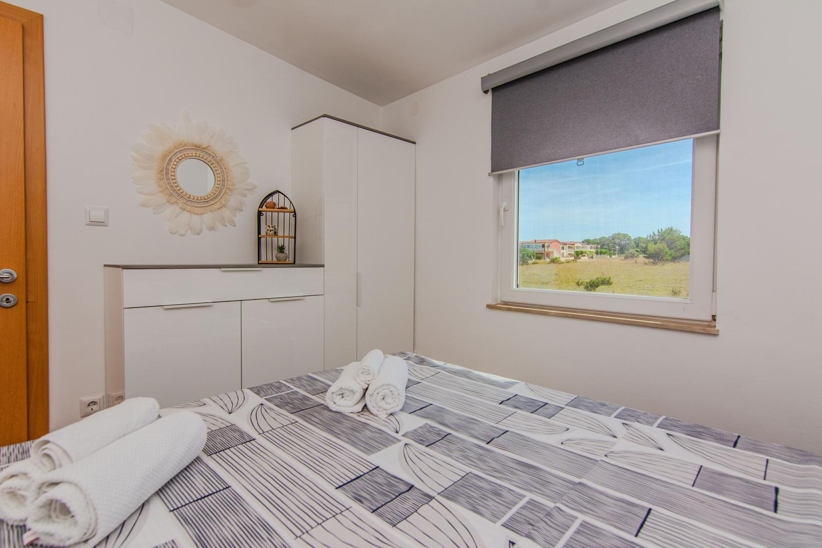 Schlafzimmer mit Bett, Schrank und Fensterblick auf Grünflächen