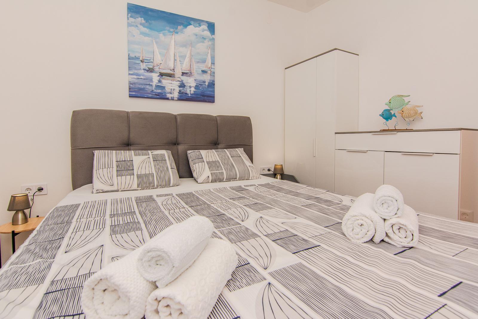 Schlafzimmer mit Bett, Kleiderschrank und Wandbild mit Segelbooten.