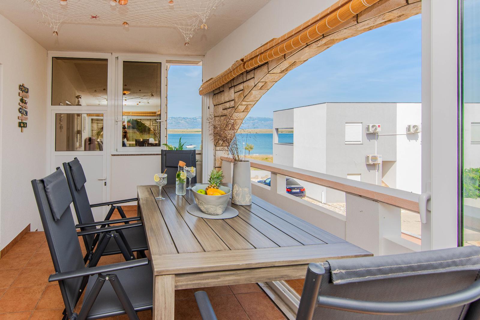 Terrasse mit Tisch und Stühlen, Blick auf das Meer und moderne Gebäude.