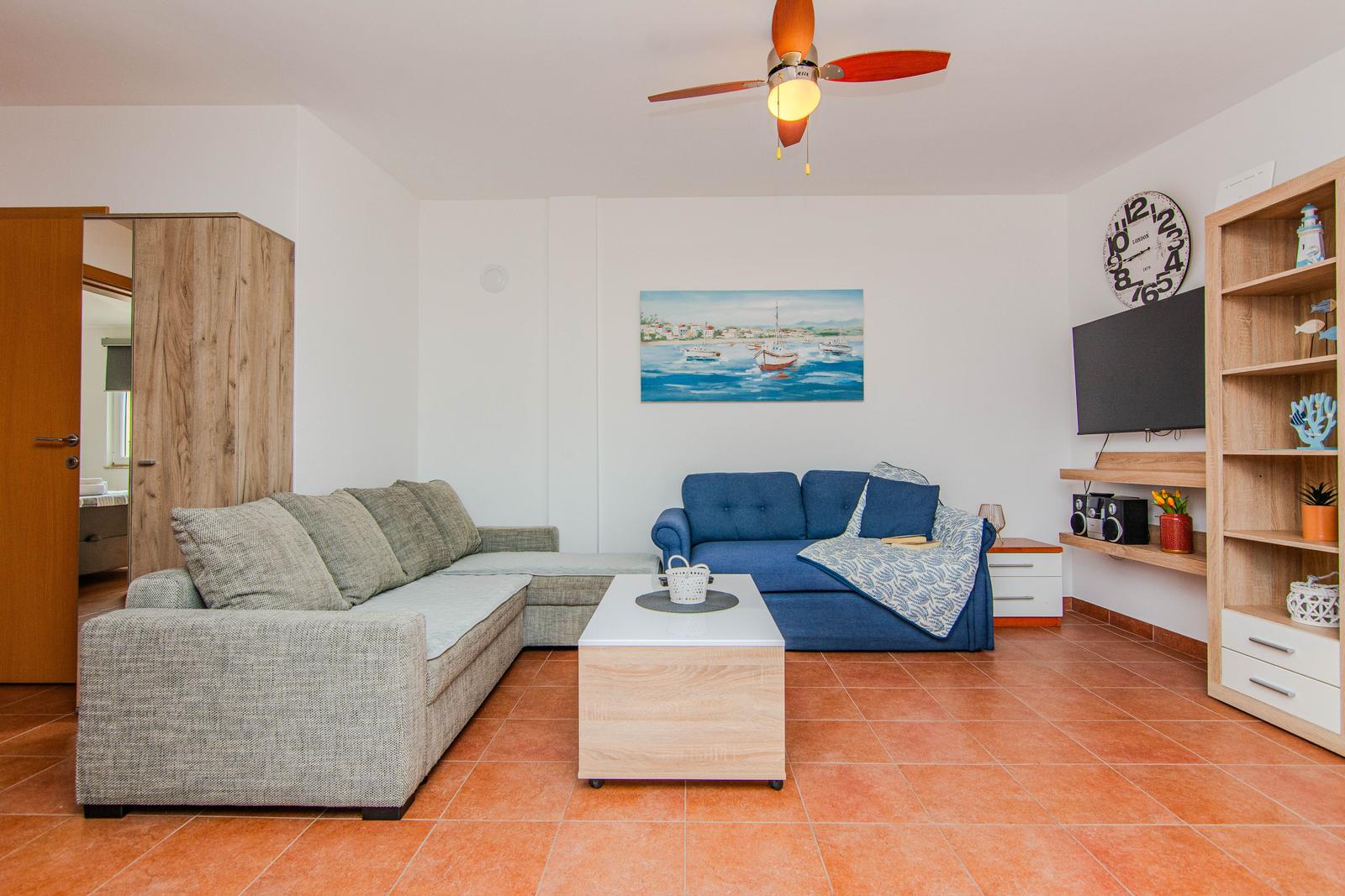 Wohnzimmer mit Sofa, Couchtisch und Fernseher an der Wand.