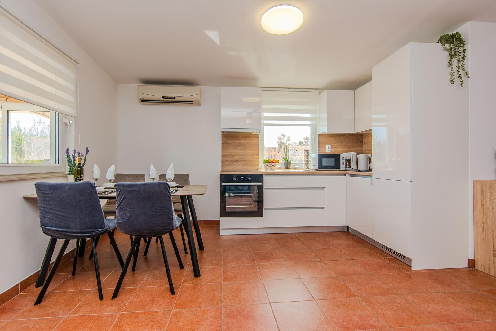 Küche mit Essbereich, weißen Schränken und Terrakottaboden.