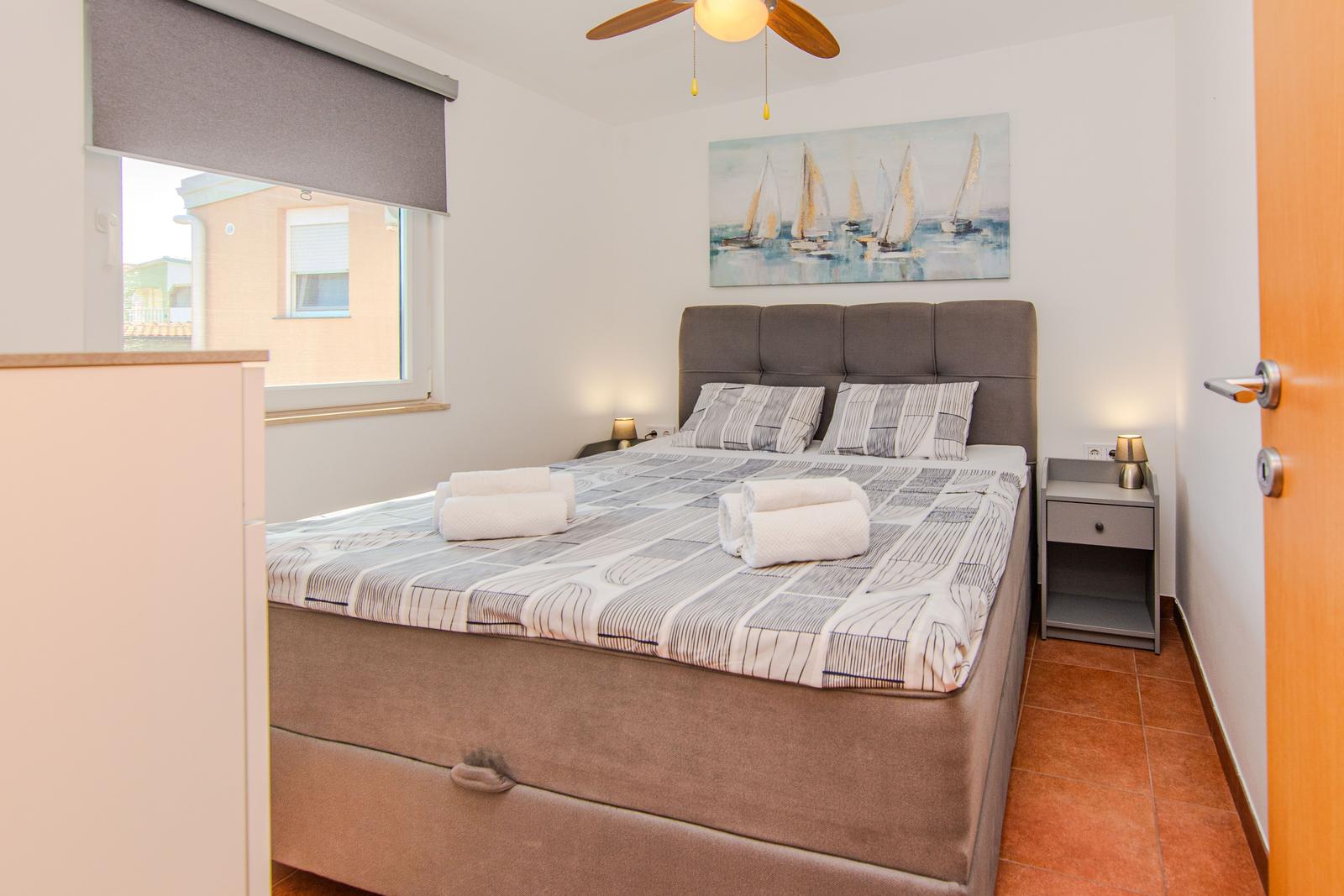 Schlafzimmer mit Bett, Nachttisch und Wandbild mit Segelbooten.