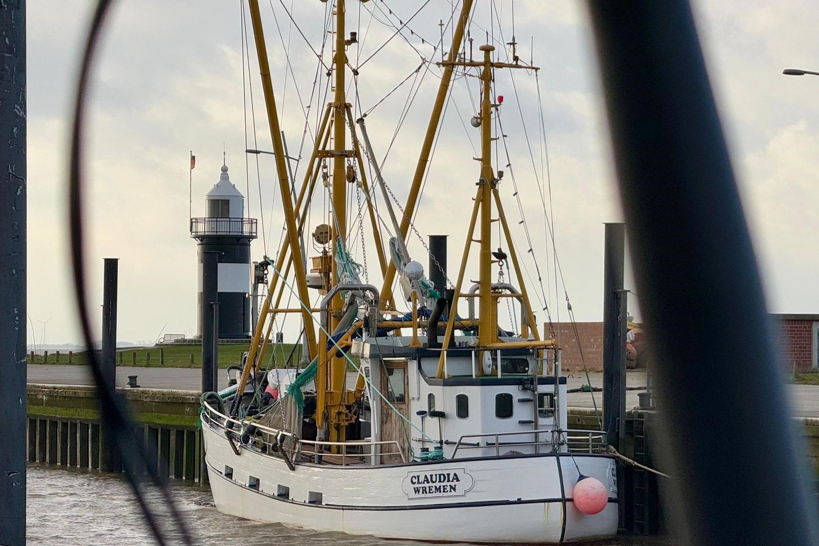 Fischerboot Claudia Wremen liegt im Hafen vor einem Leuchtturm.