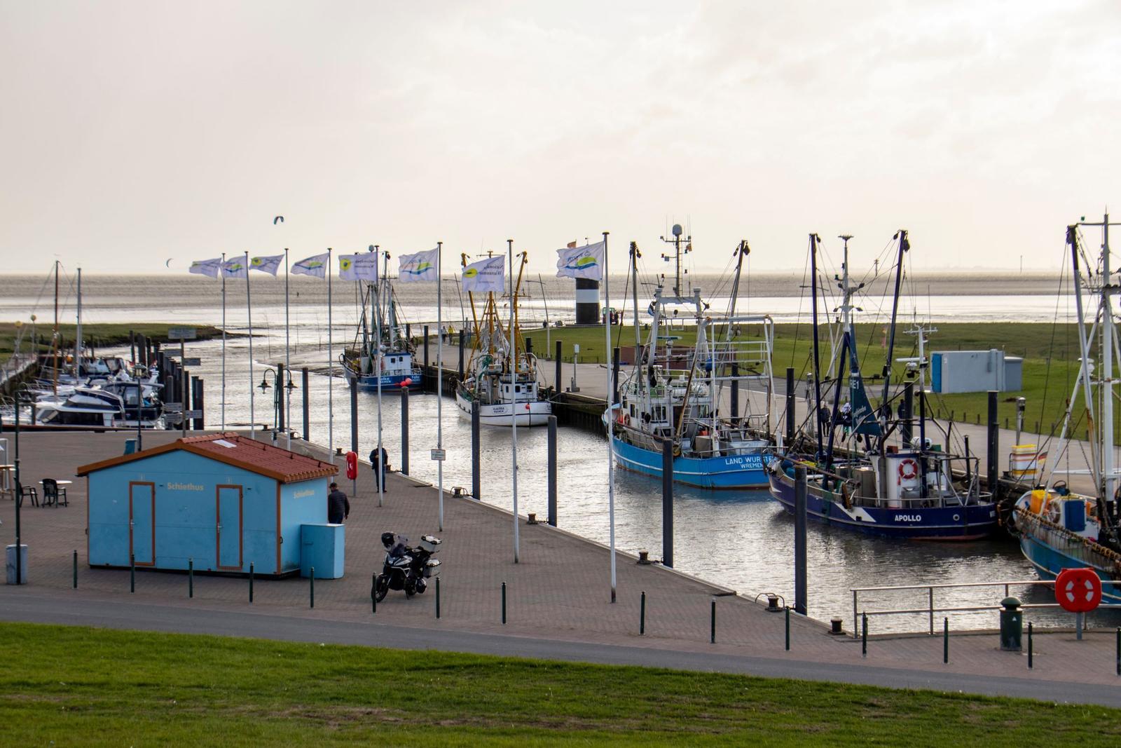 Hafen mit Fischerbooten und blauem Schießhaus an der Uferpromenade.