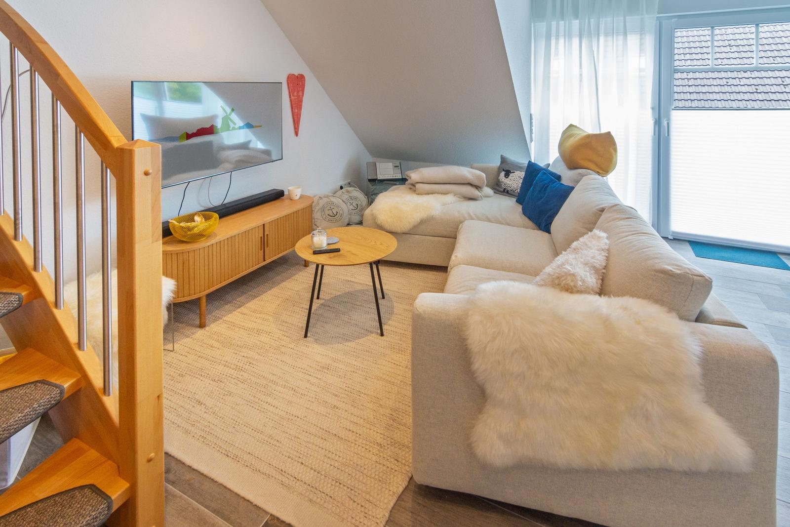 Wohnzimmer mit Sofa, Fernseher und Holztreppe