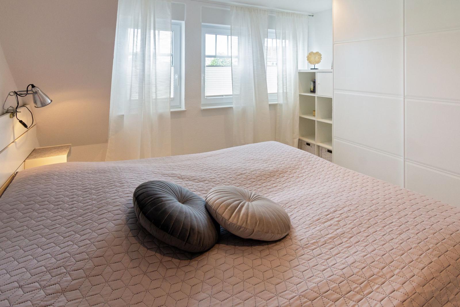 Schlafzimmer mit Bett, zwei Kissen, Fenster und Schrank.