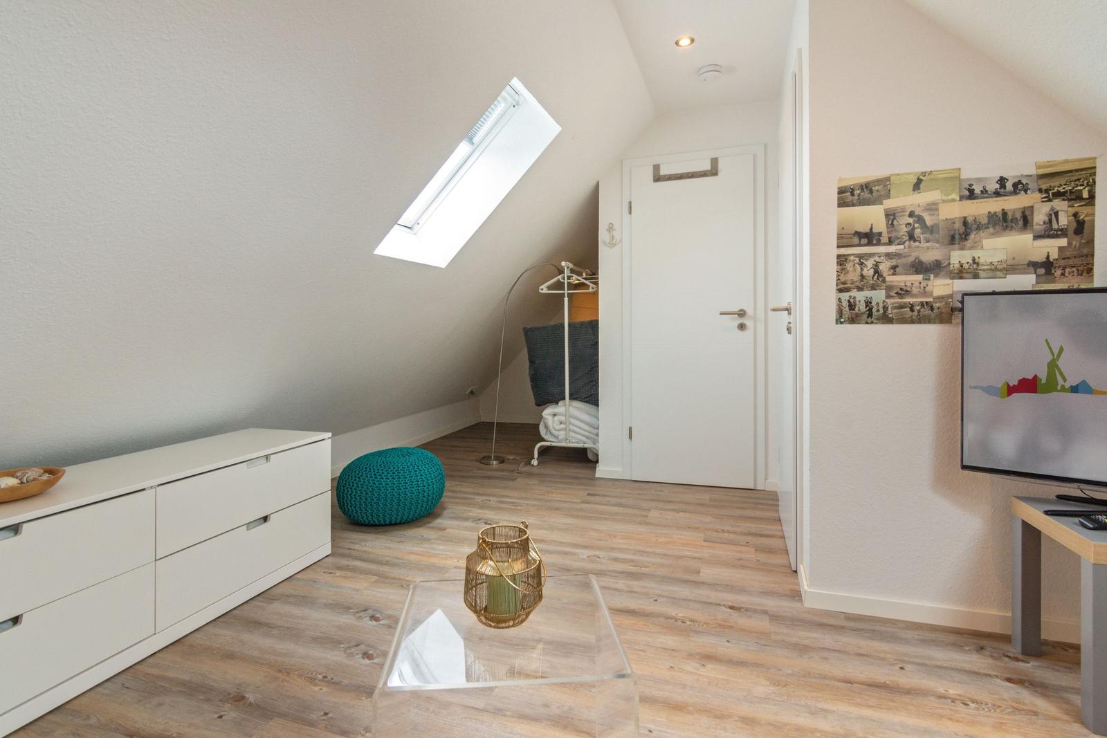 Schlafzimmer mit Dachschrägen, Fenster, Schrank und Fernseher.