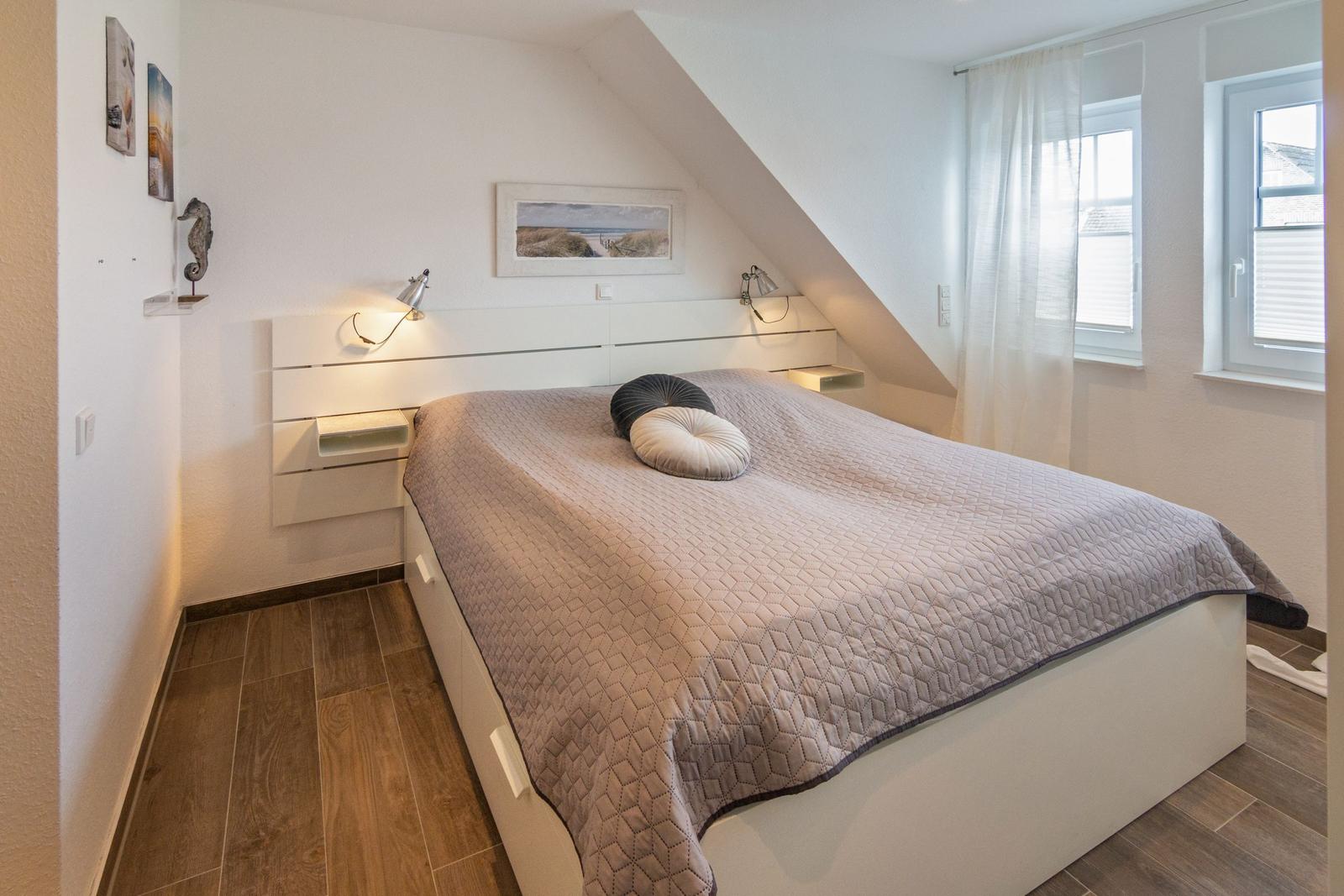 Schlafzimmer mit Dachschräge, Bett, Fenster und Wanddekoration.