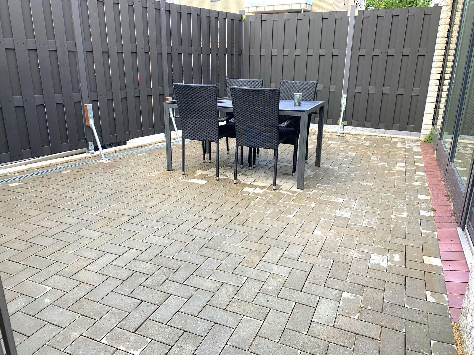Terrasse mit Tisch und Stühlen, umgeben von dunklem Holzzaun.