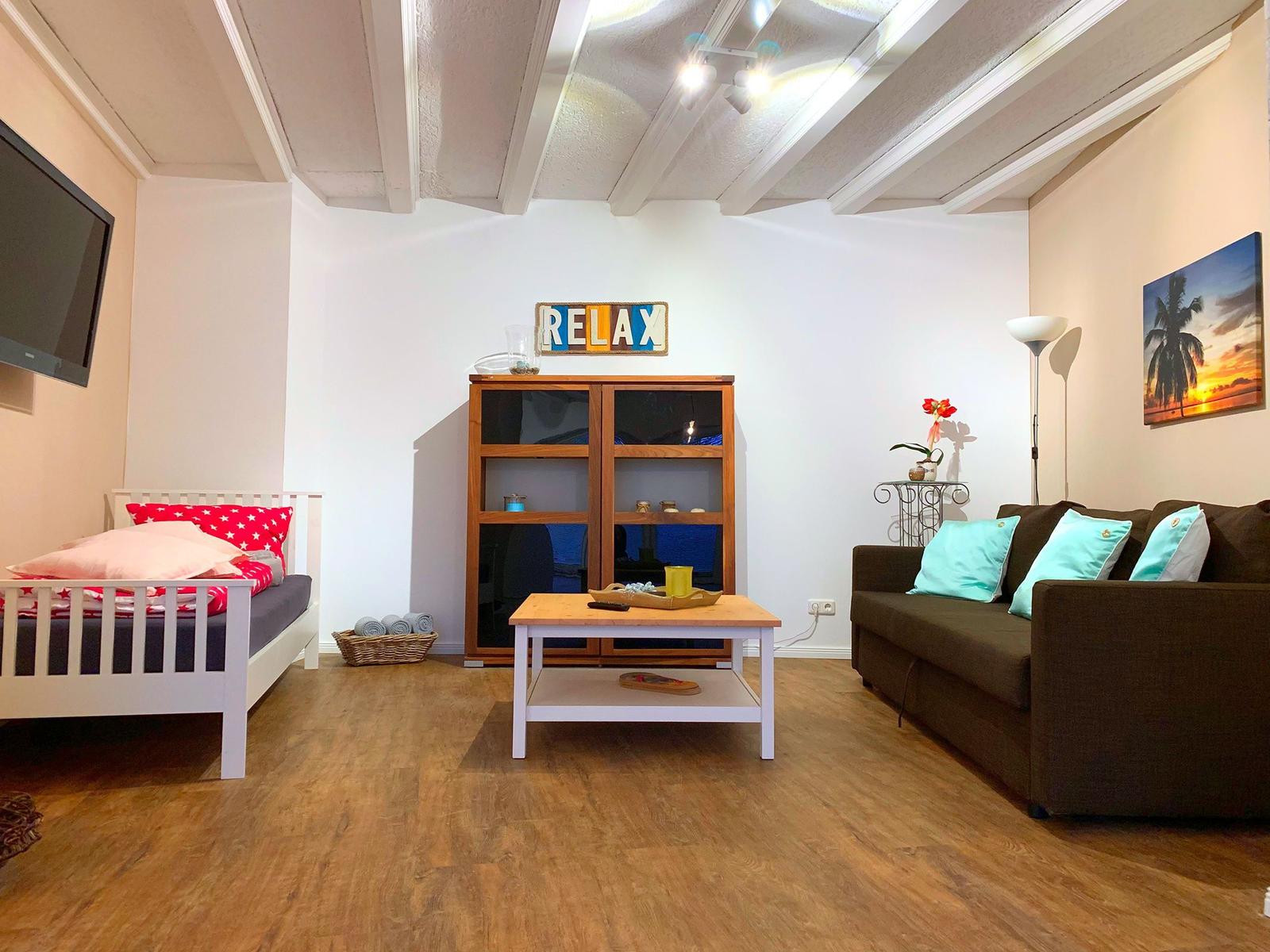 Wohnzimmer mit Sofa, Bett und Holzboden. Decke mit Balken.