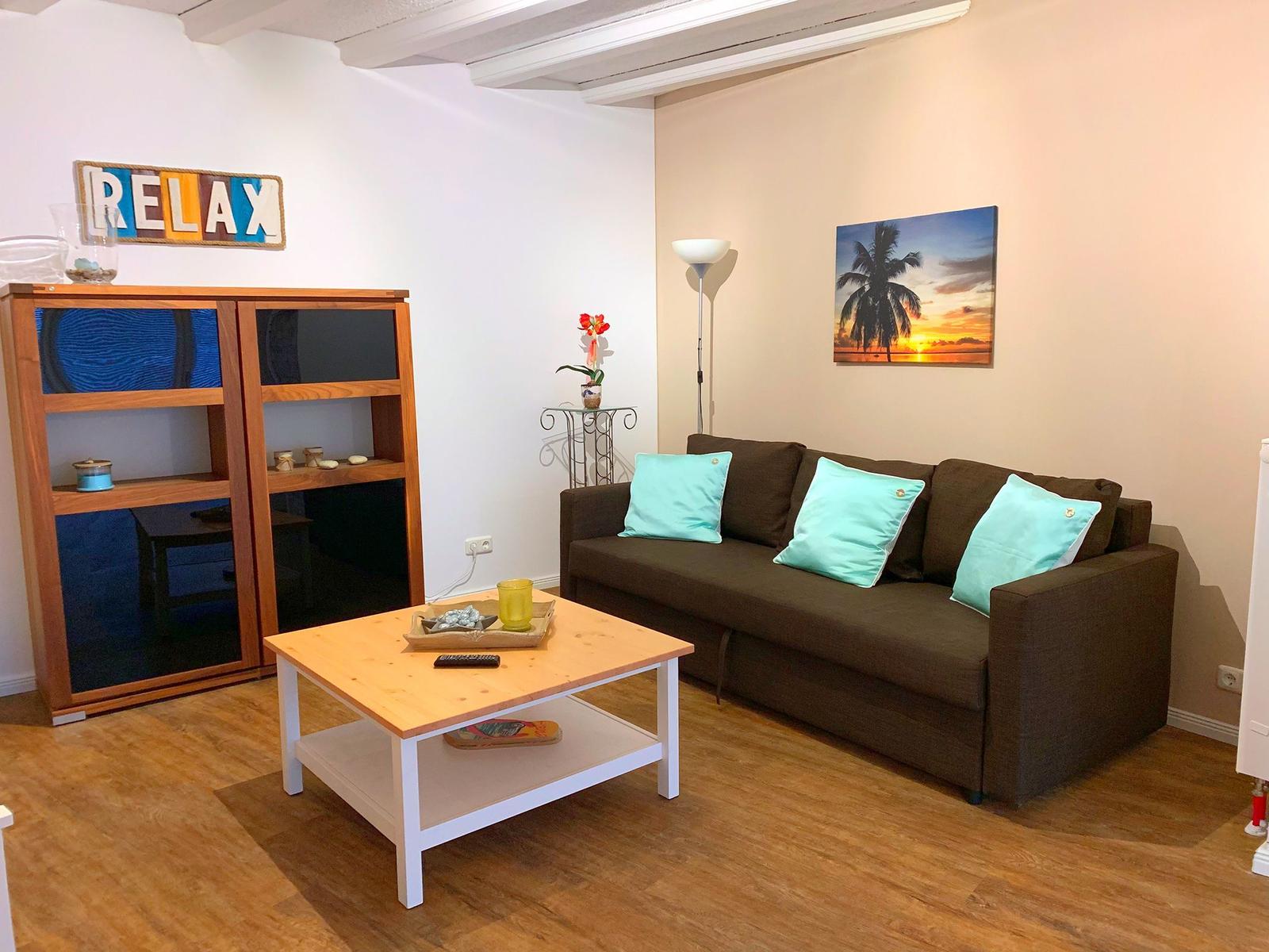 Ein Wohnzimmer mit braunem Sofa, türkisen Kissen und Holzboden.