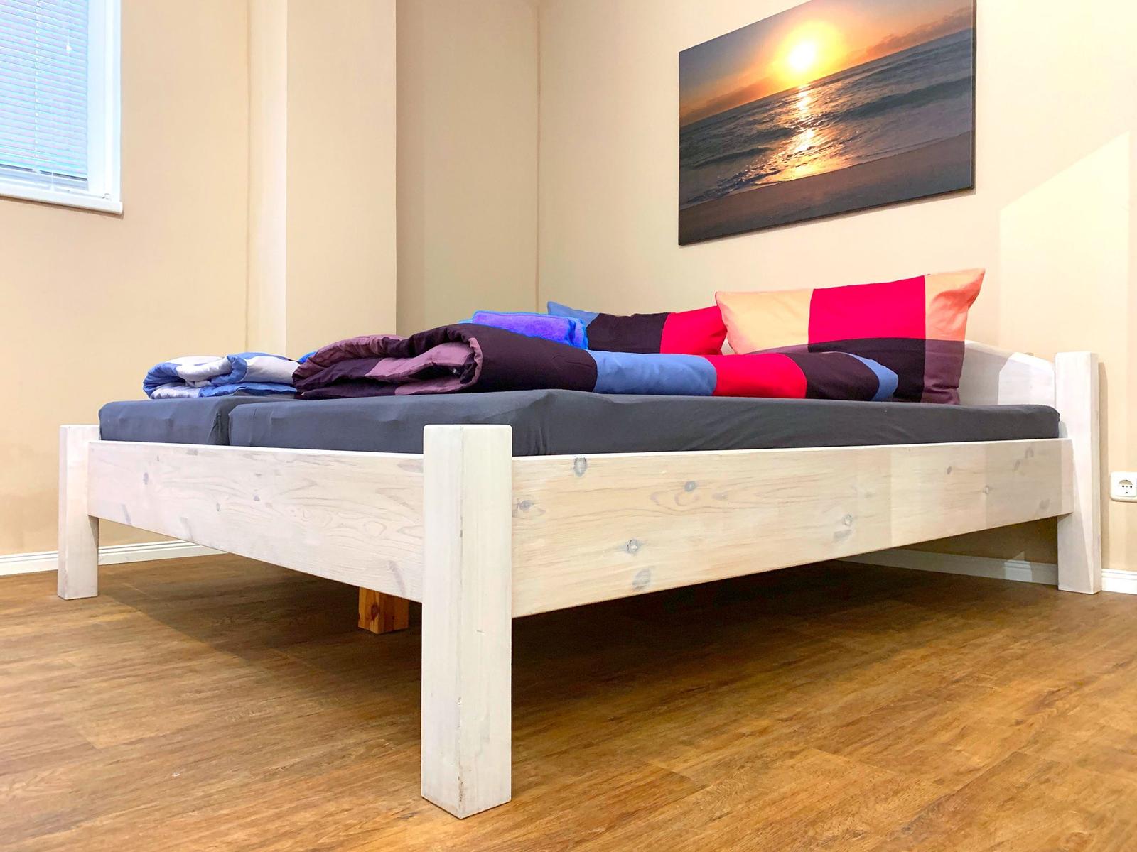 Ein Bett mit Holzrahmen, bunten Kissen und einer Wanddekoration.