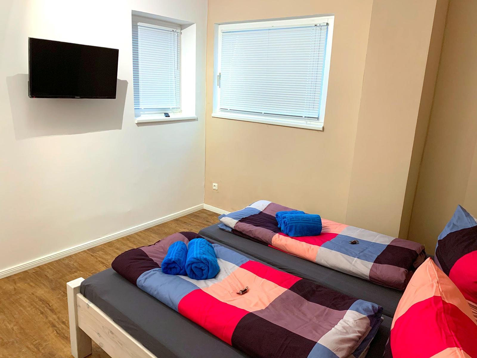 Zwei Betten mit bunten Bettwäschen, TV und Fenster mit Jalousien.