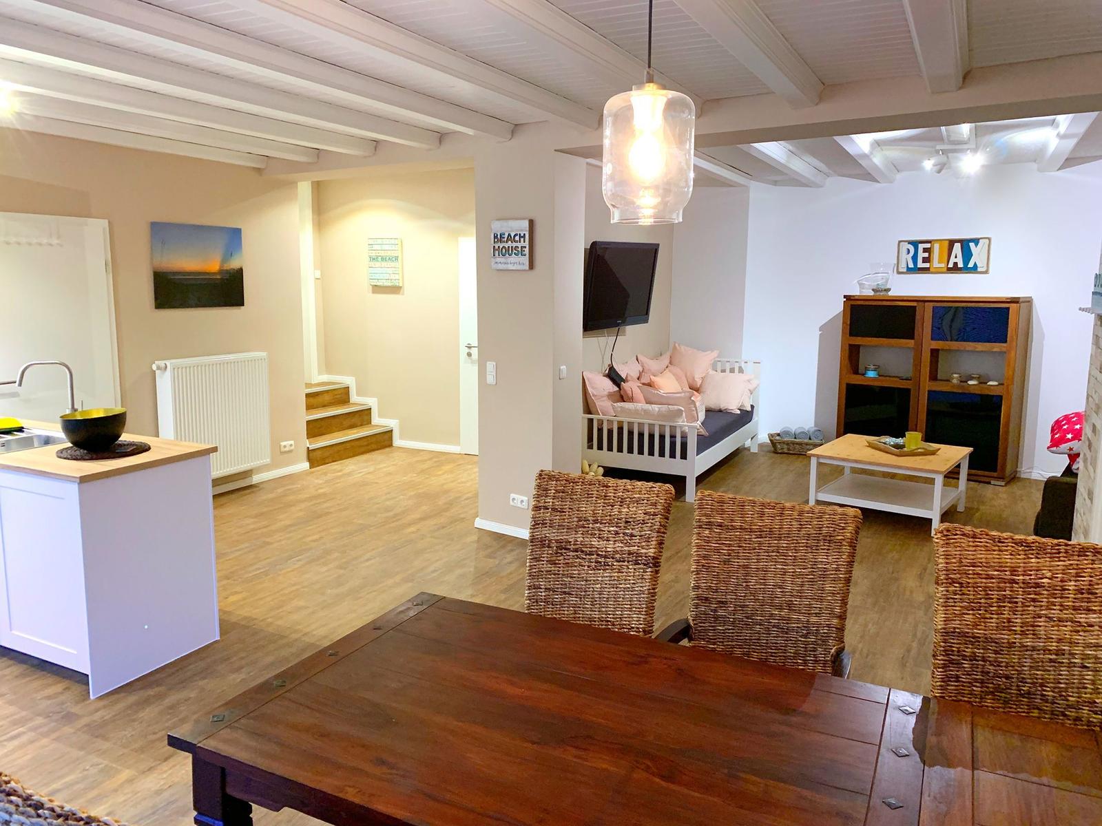 Wohnküche mit Esstisch, Sofa und Fernseher. Holzboden und Deckenbalken.