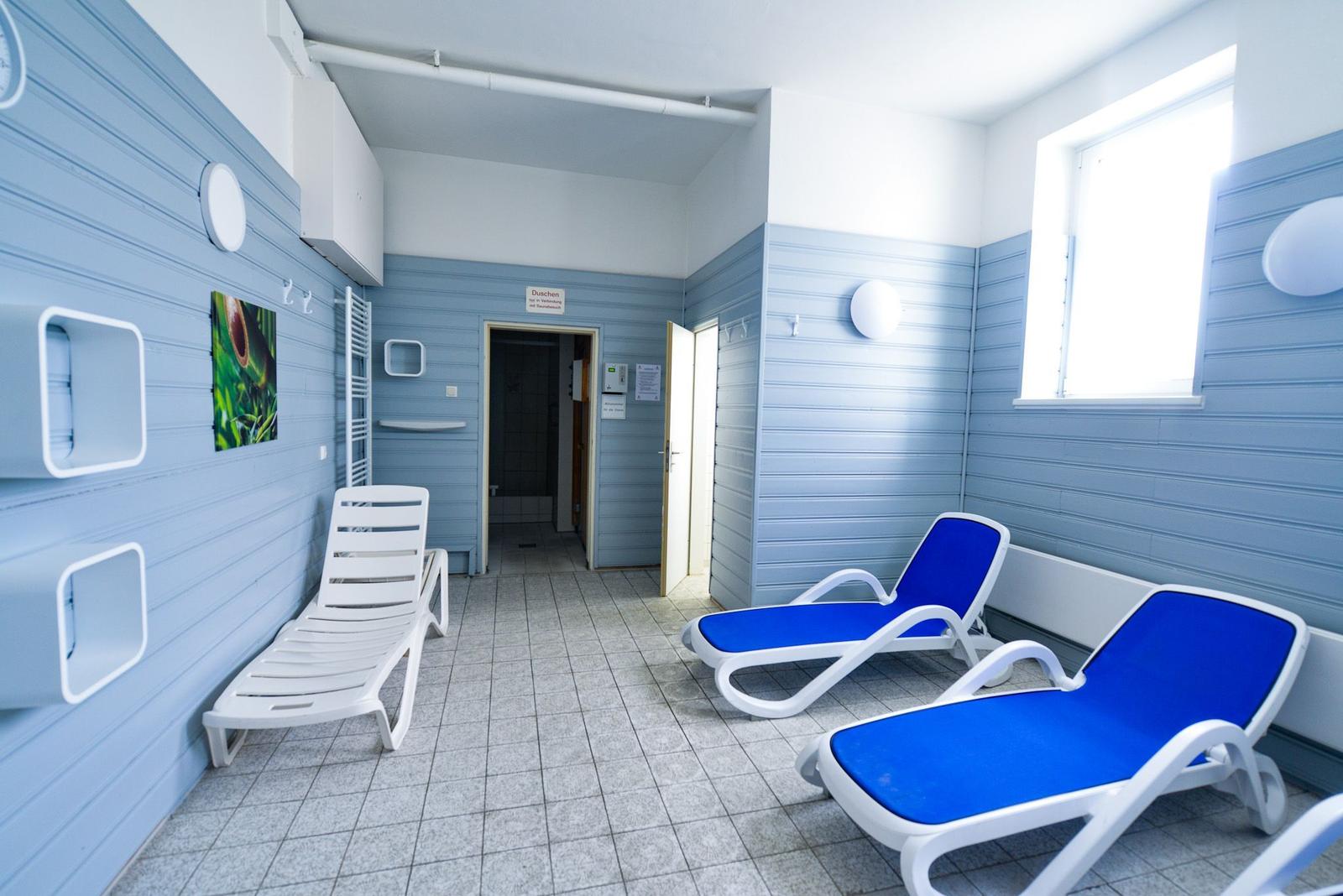 Raum mit blauen Wänden, Liegen und Dusche im Hintergrund.