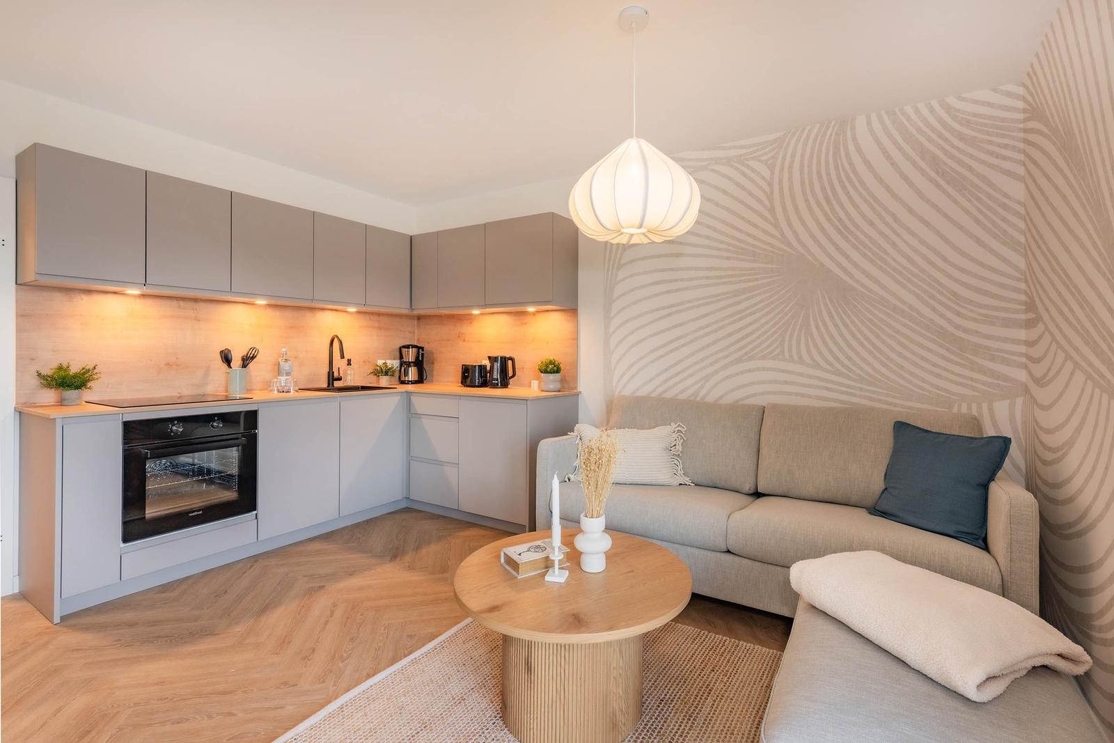 Küche mit Arbeitsplatte, Herd und Kühlschrank. Wohnbereich mit Sofa und runden Tisch.