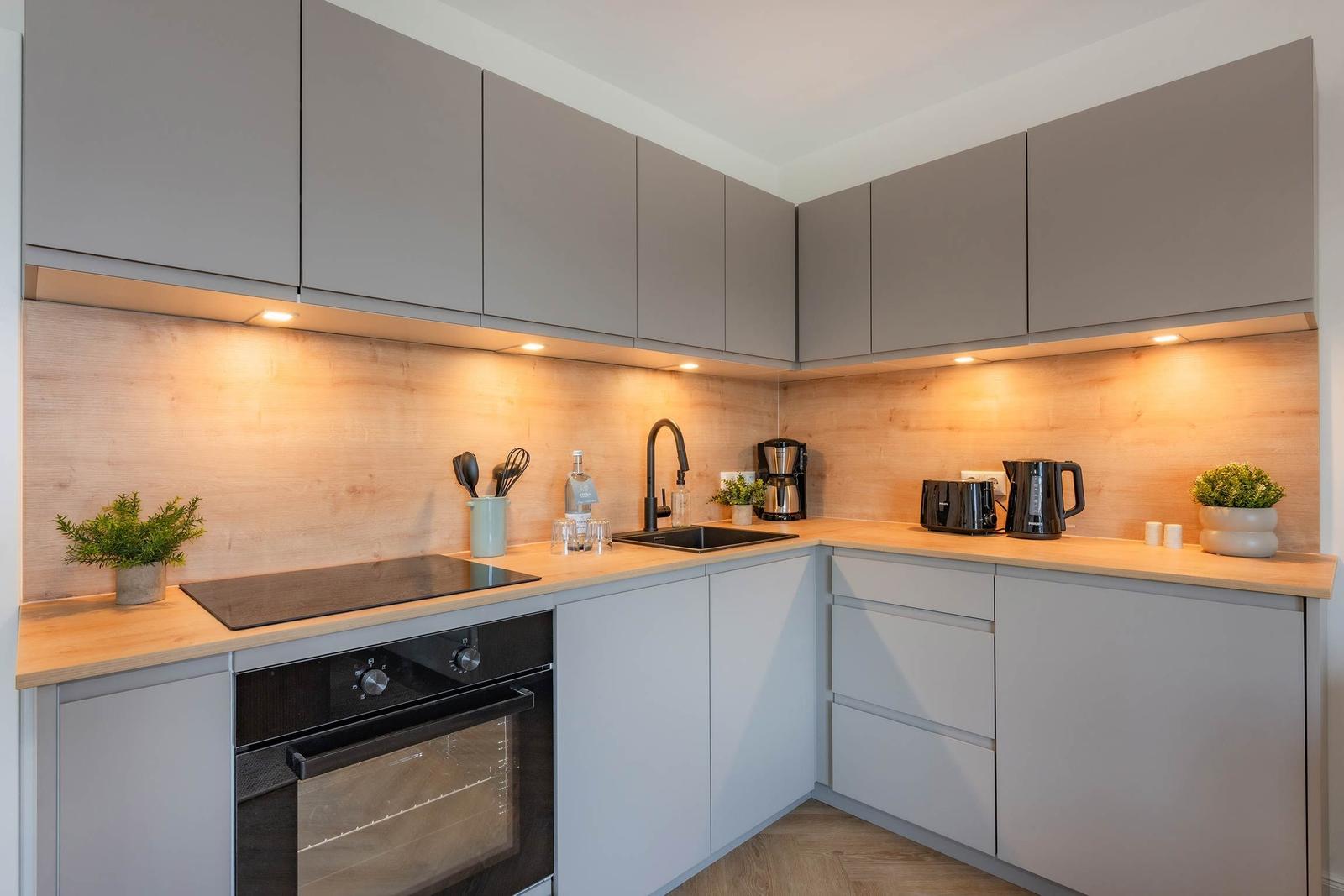 Moderne Küche mit grauen Schränken, Holzoberfläche und integriertem Backofen.