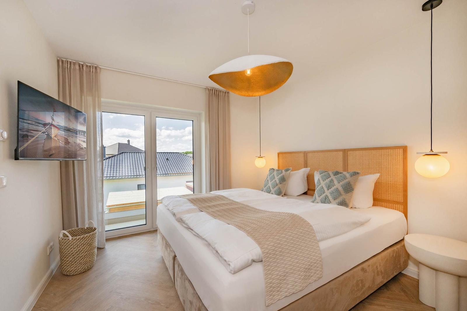 Schlafzimmer mit Doppelbett, TV und Balkonansicht.