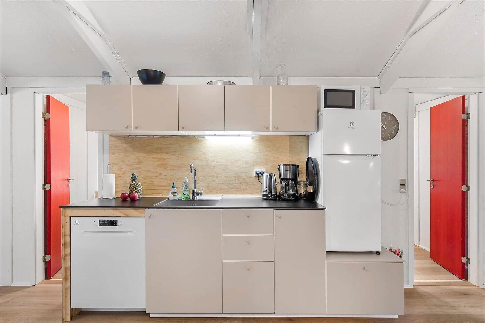 Küche mit Kühlschrank, Spüle und Geschirrspüler. Rote Türen sind sichtbar.