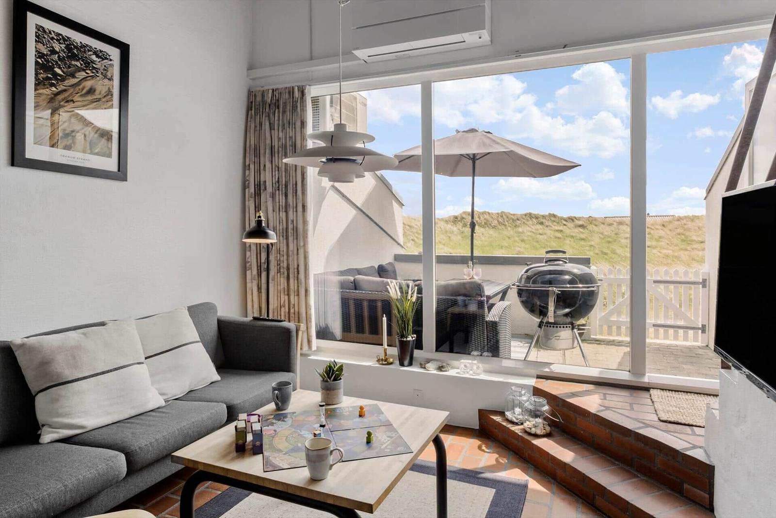 Living room with sofa, table, and view of balcony with grill and umbrella.