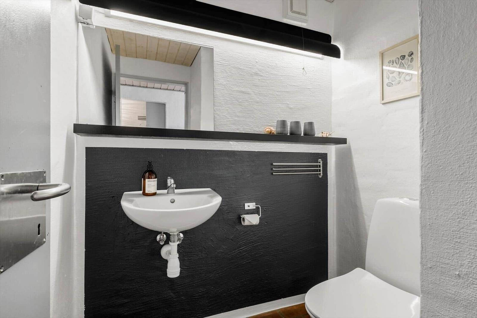 Bathroom with sink, mirror, and toilet against black and white walls.