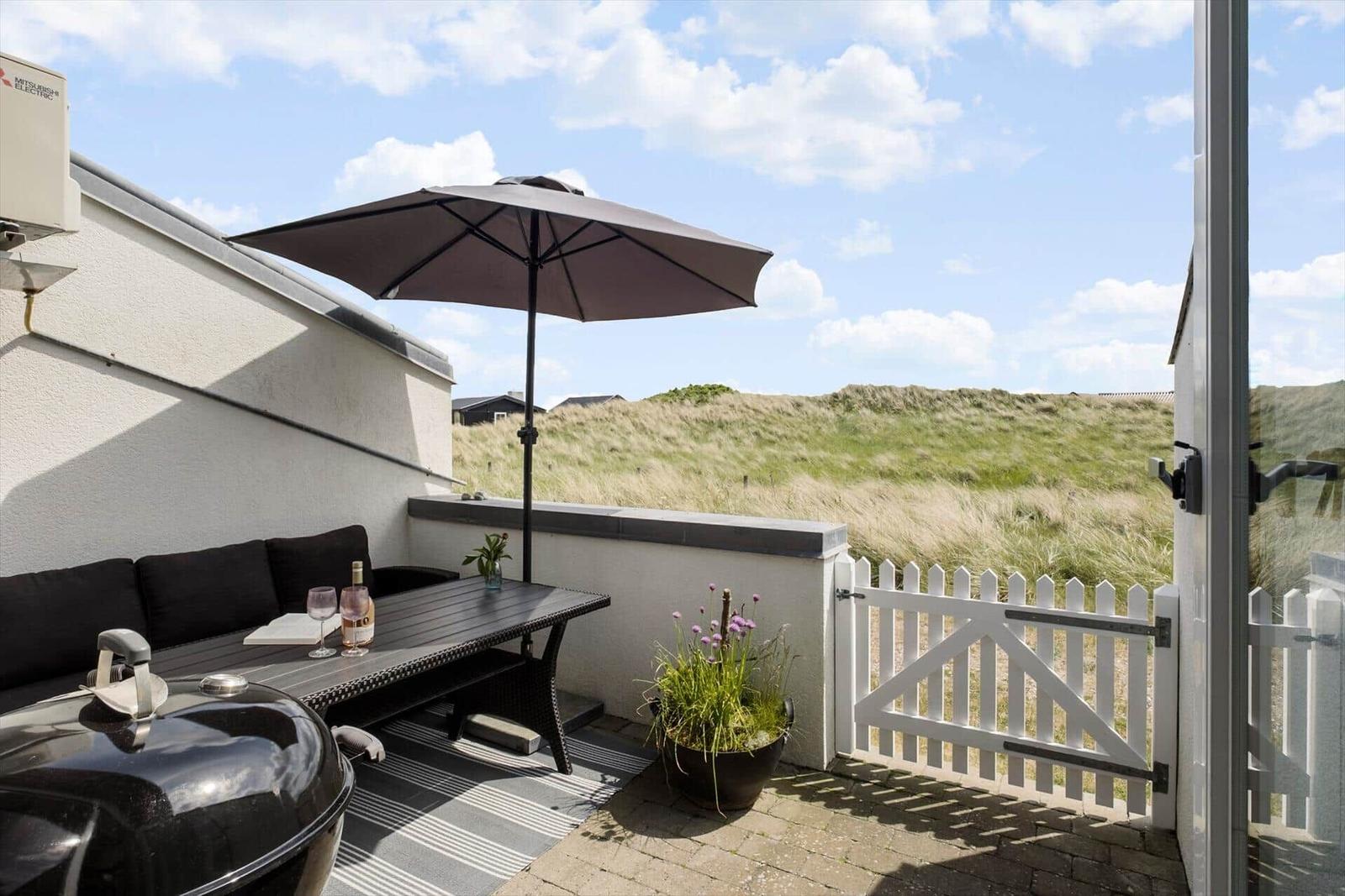 Terrace with table, bench, umbrella, and grill. View of grassy landscape.