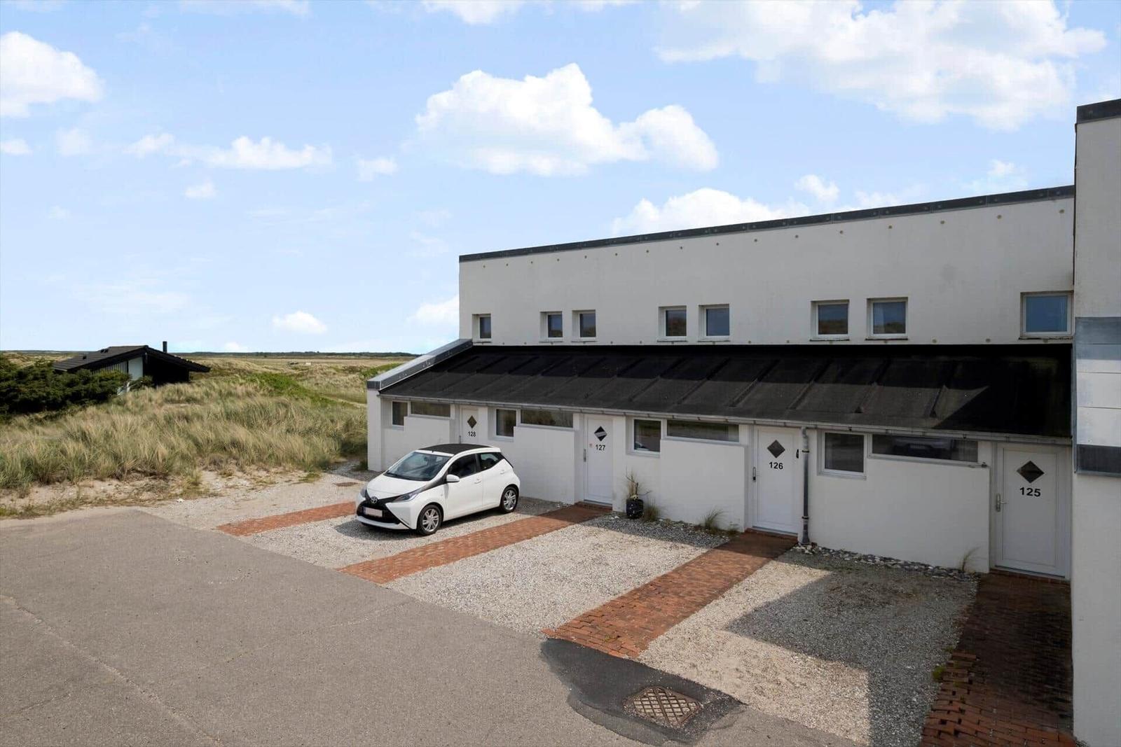 Modern white vacation apartments with parking spots and dune views.