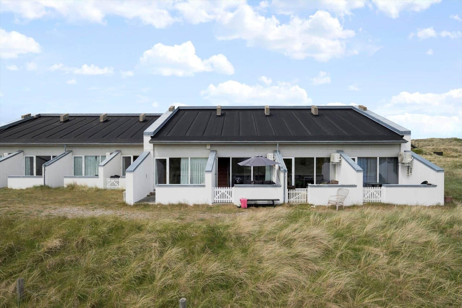 House with terrace and white fence in front of grassland under blue sky.