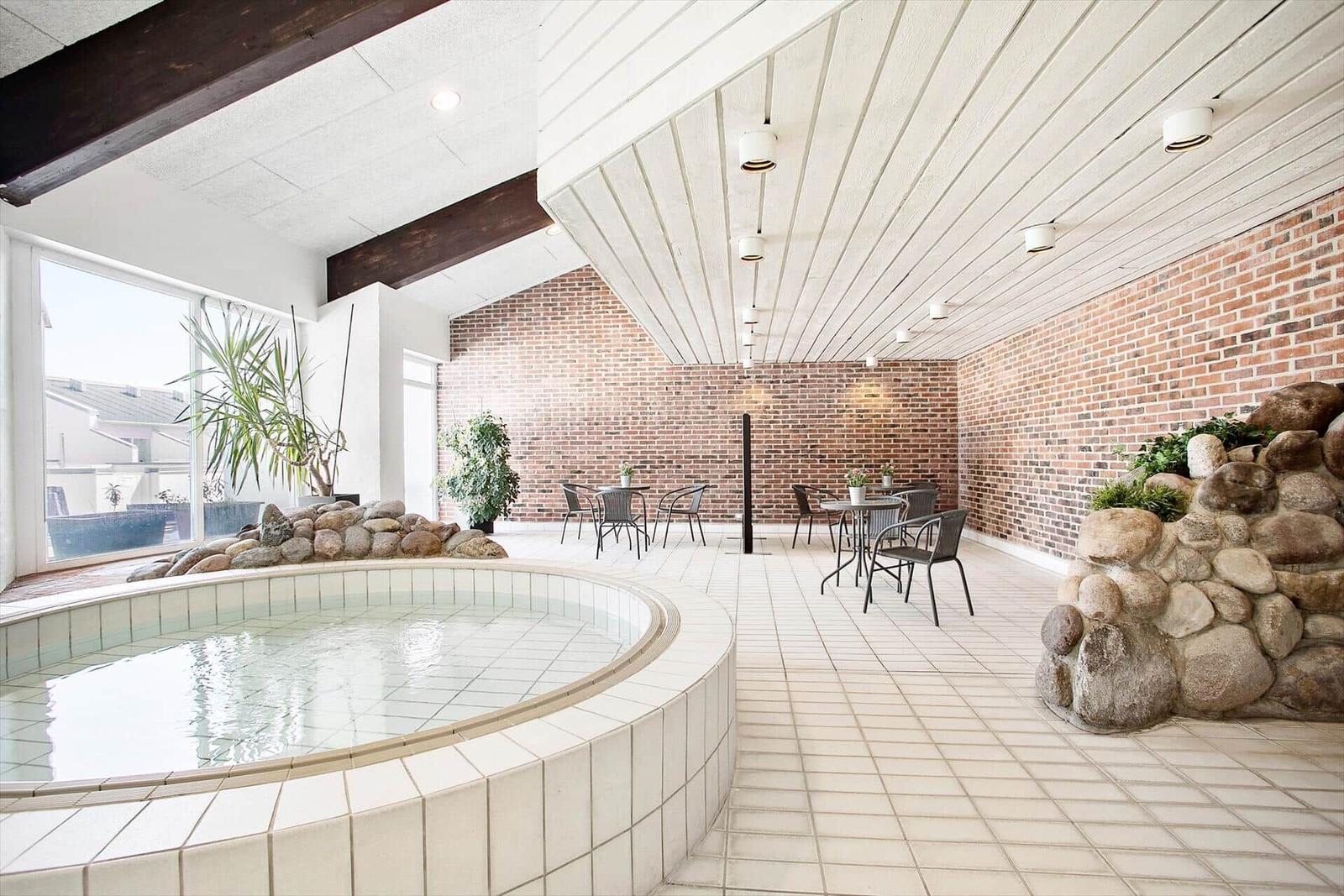Indoor pool with stone surround and seating area against brick wall.
