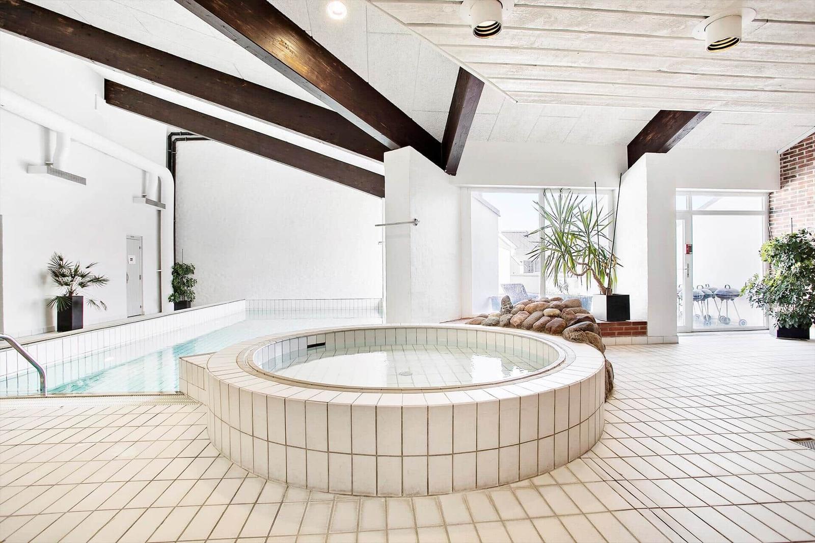 Indoor pool with round hot tub and wooden beam ceiling.