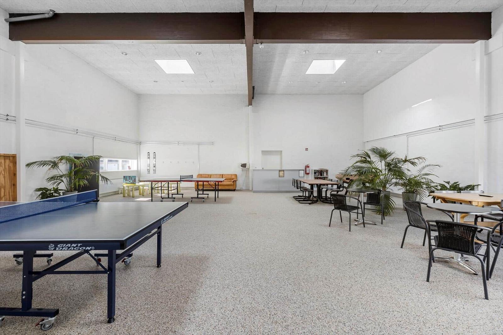 Large room with ping pong tables, seating, and plants.