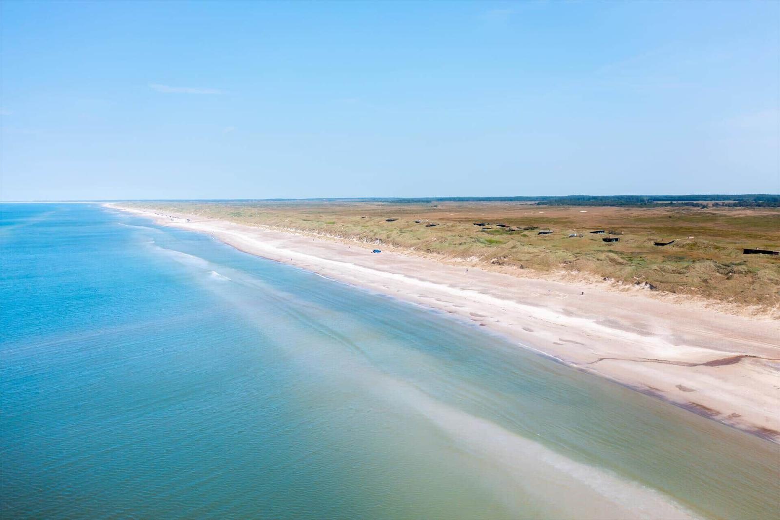 Beach with dunes and calm sea under blue sky