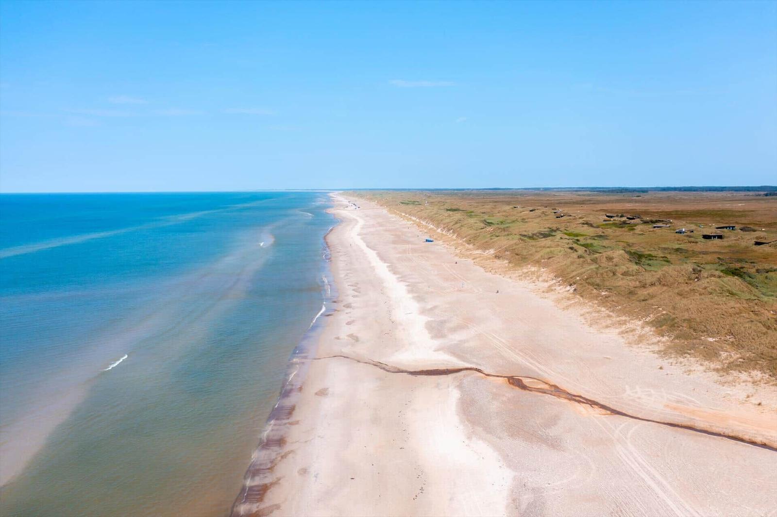 Long beach stretch with dunes and sea under blue sky.