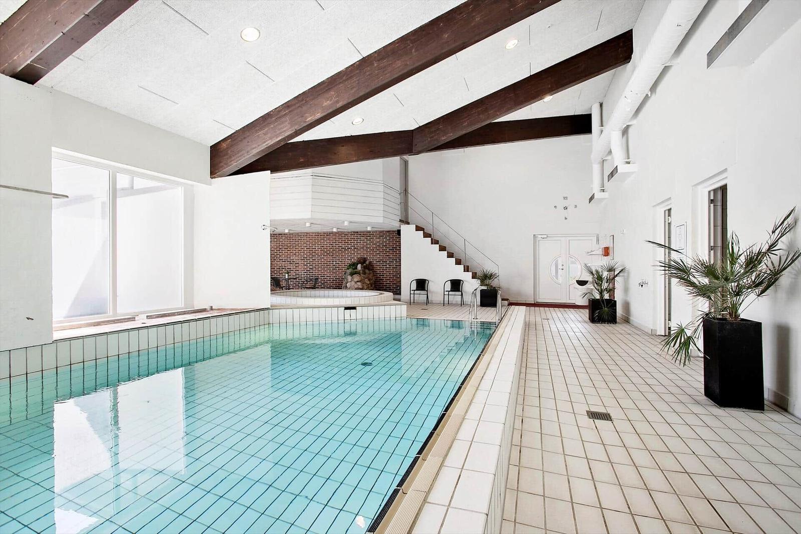Indoor pool with sauna and staircase. White walls and wooden beams.