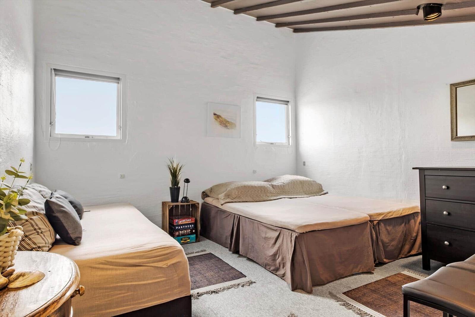 Two beds, two windows, white walls, dark dresser, and wooden beams on ceiling.