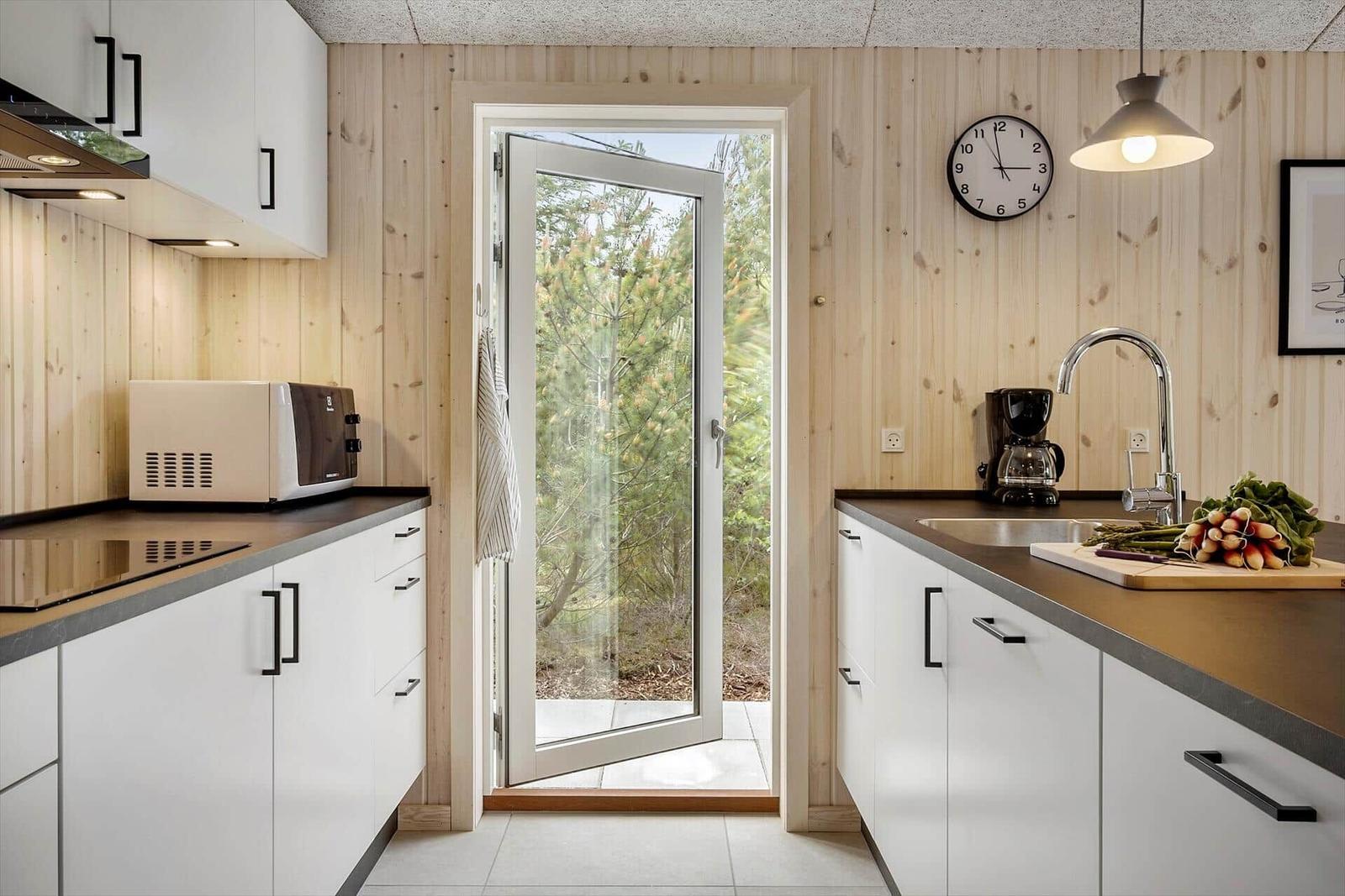 Küche mit Holzwand, Tür zum Garten und Arbeitsfläche mit Gemüse.