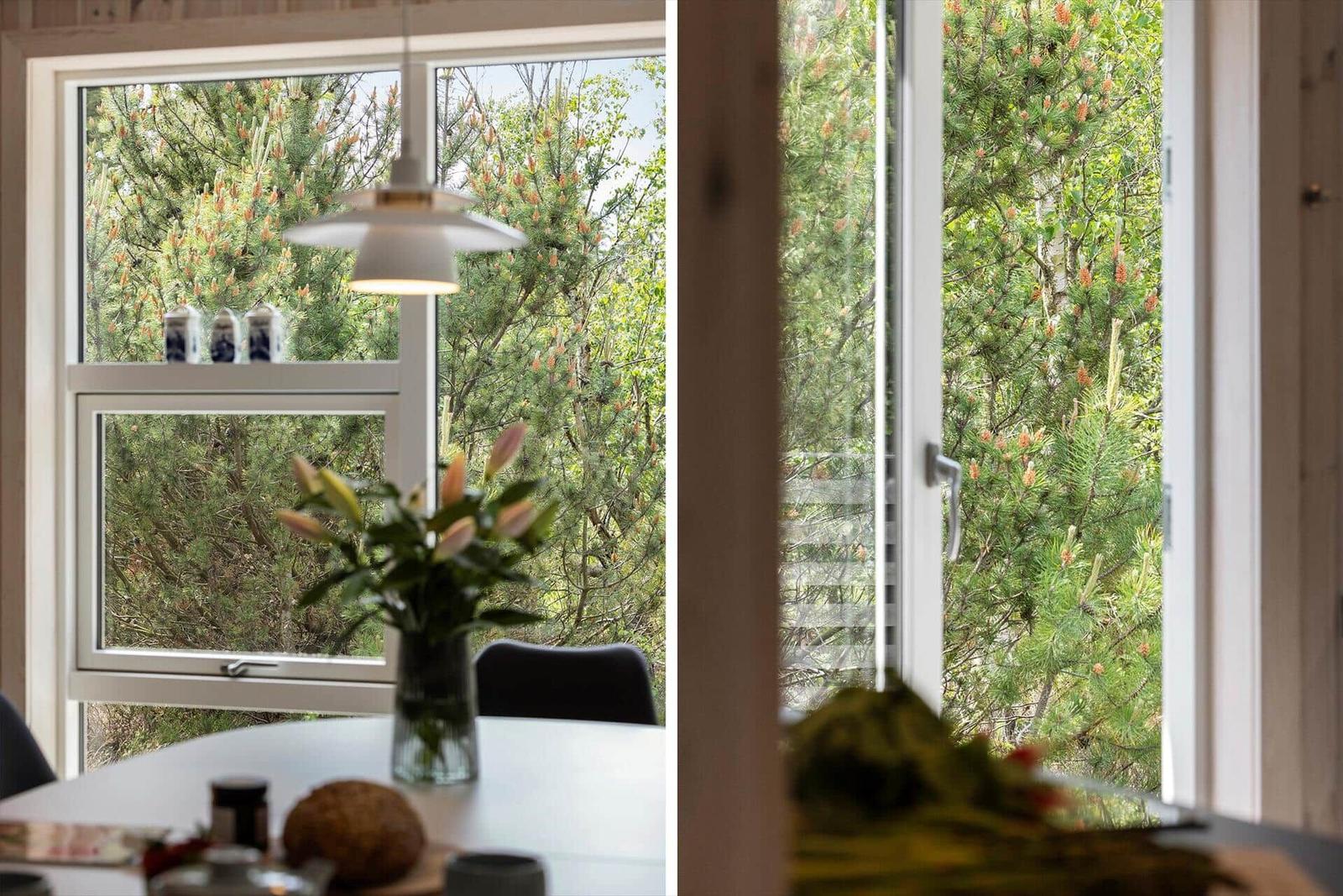 Durch Fenster blickt man auf grüne Bäume. Tisch mit Blumen und Keramik.