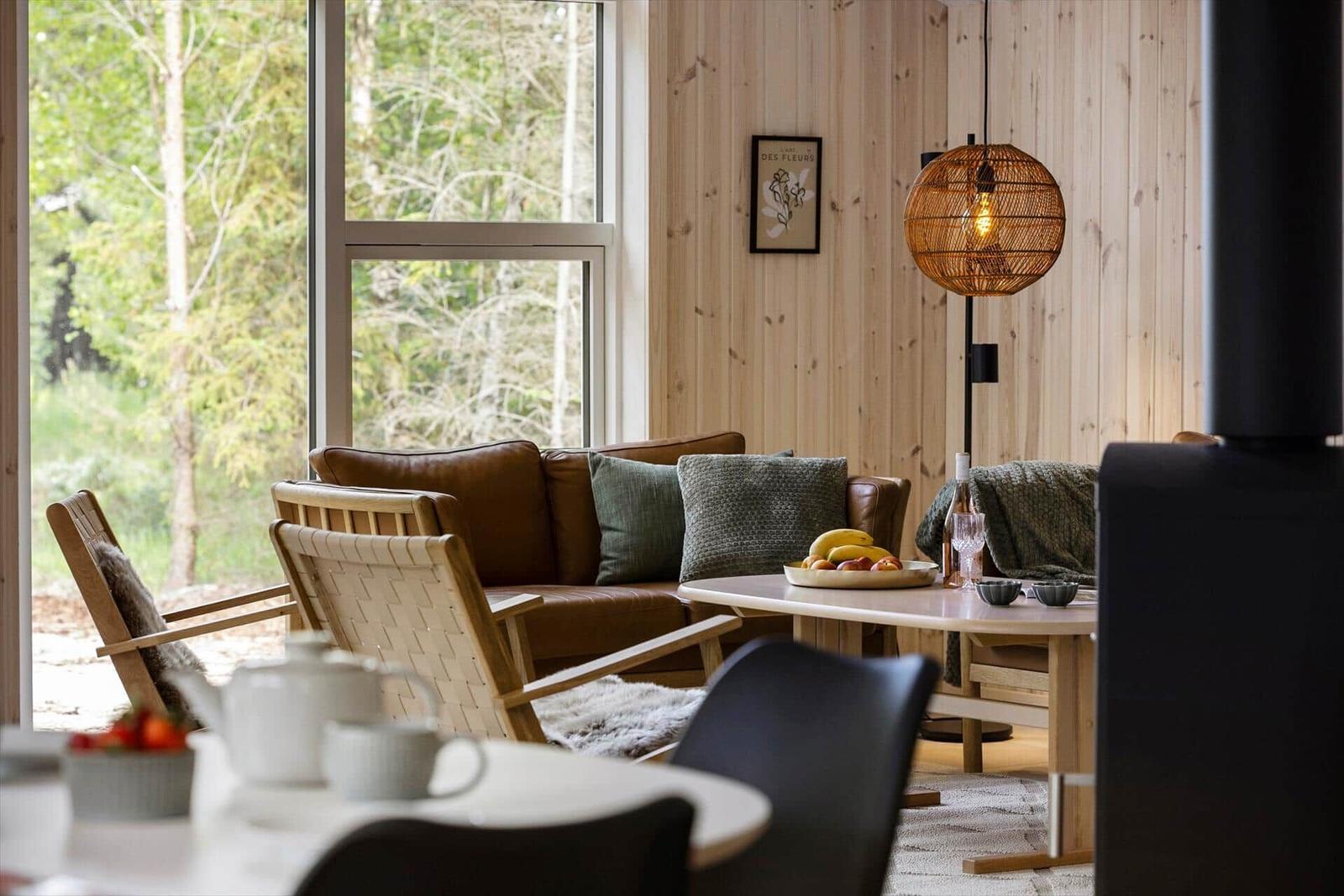 Wohnzimmer mit Holzwand, Sofa, Tisch und Blick auf Wald.