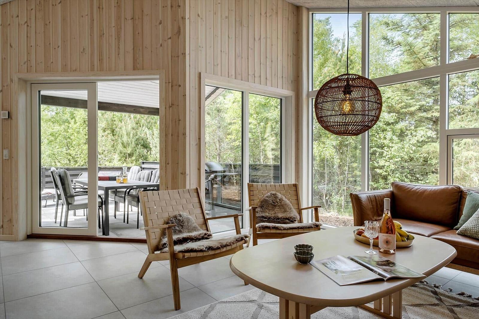 Wohnzimmer mit Holzwand, Glasfront und braunem Sofa. Tisch mit Getränken und Zeitschriften.