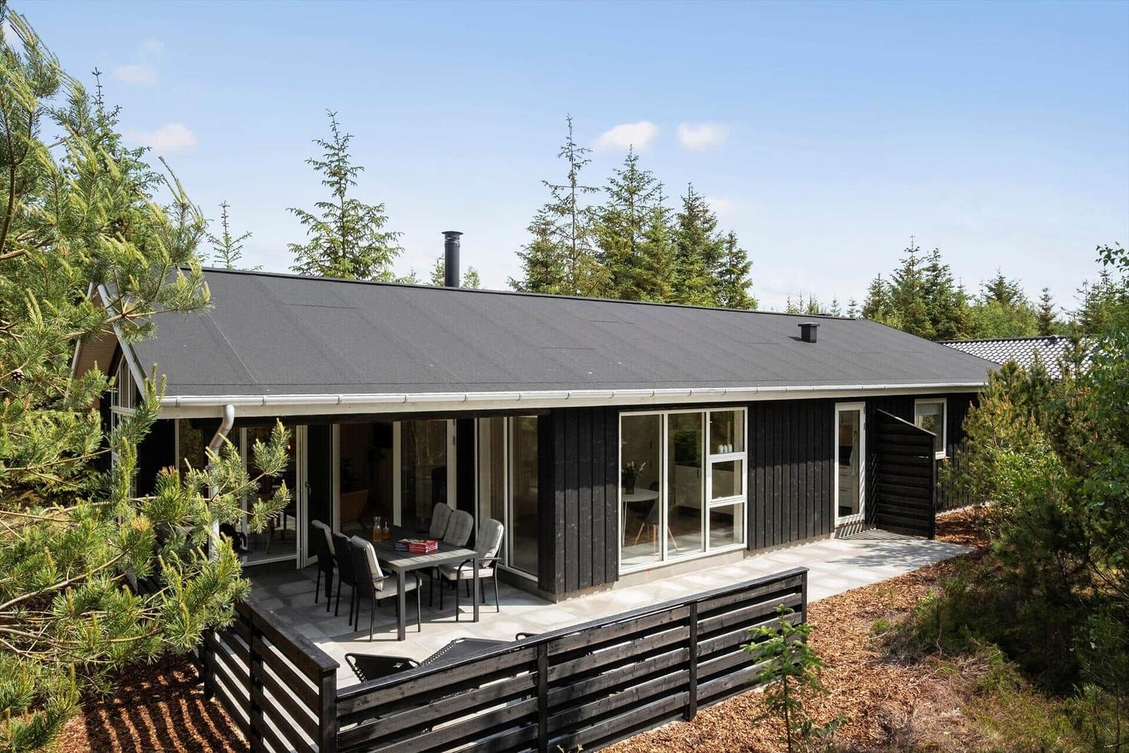Moderne Holzhütte mit Terrasse und Sitzgelegenheiten im Wald.